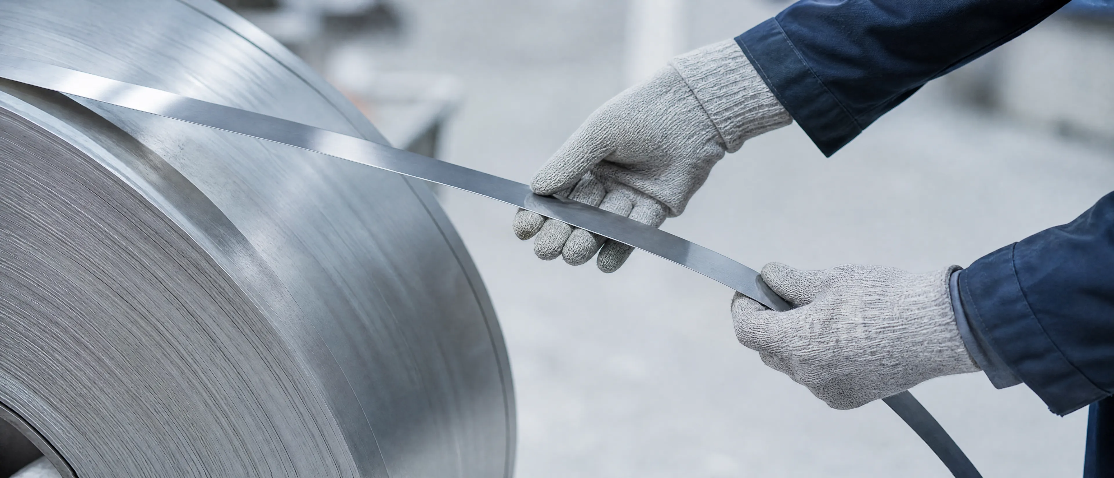 Hände in Arbeitshandschuhen führen die Kante eines schmalen Stahlbands